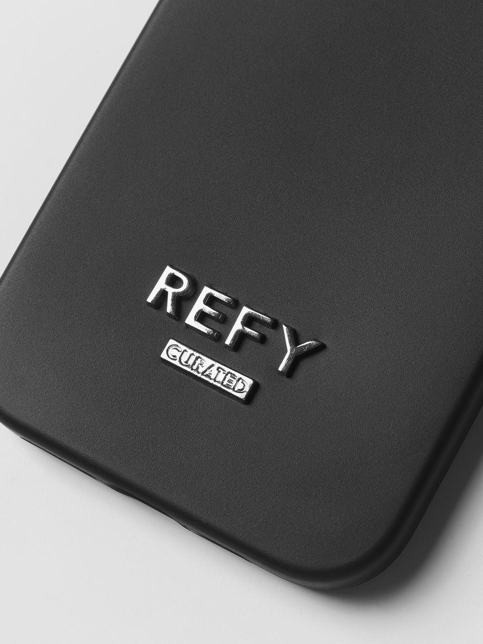 CLOSE UP IMAGE OF METAL REFY CURATED LOGO TO BACK OF PHONE CASE